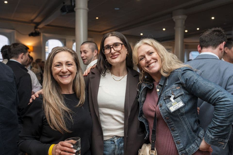 Three guests with drinks, arms around each other, in a crowded upstairs bar