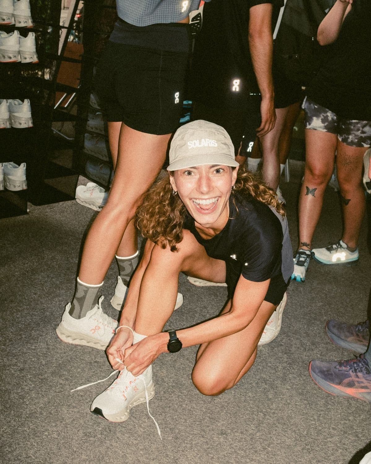 A runner crouching to tie her shoelace, smiling, in a busy store before a run