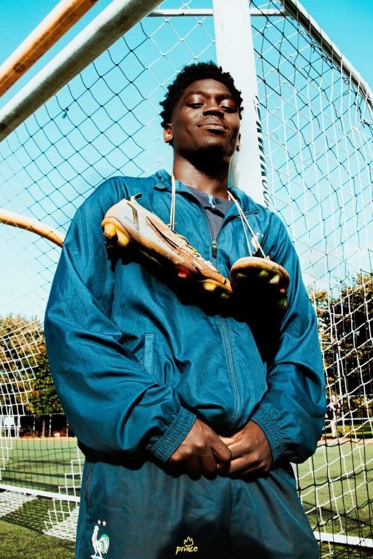 A goalkeeper leaning against the goalpost with his boots slung over his shoulder