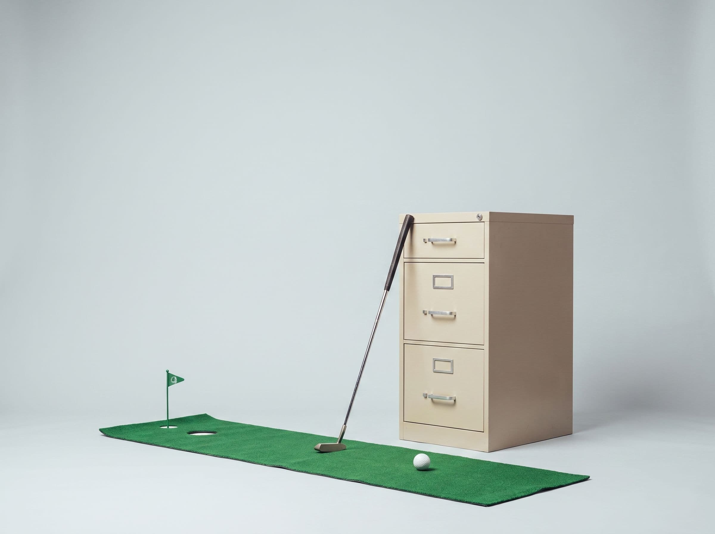 A putting mat and golf ball laid out beside an office filing cabinet